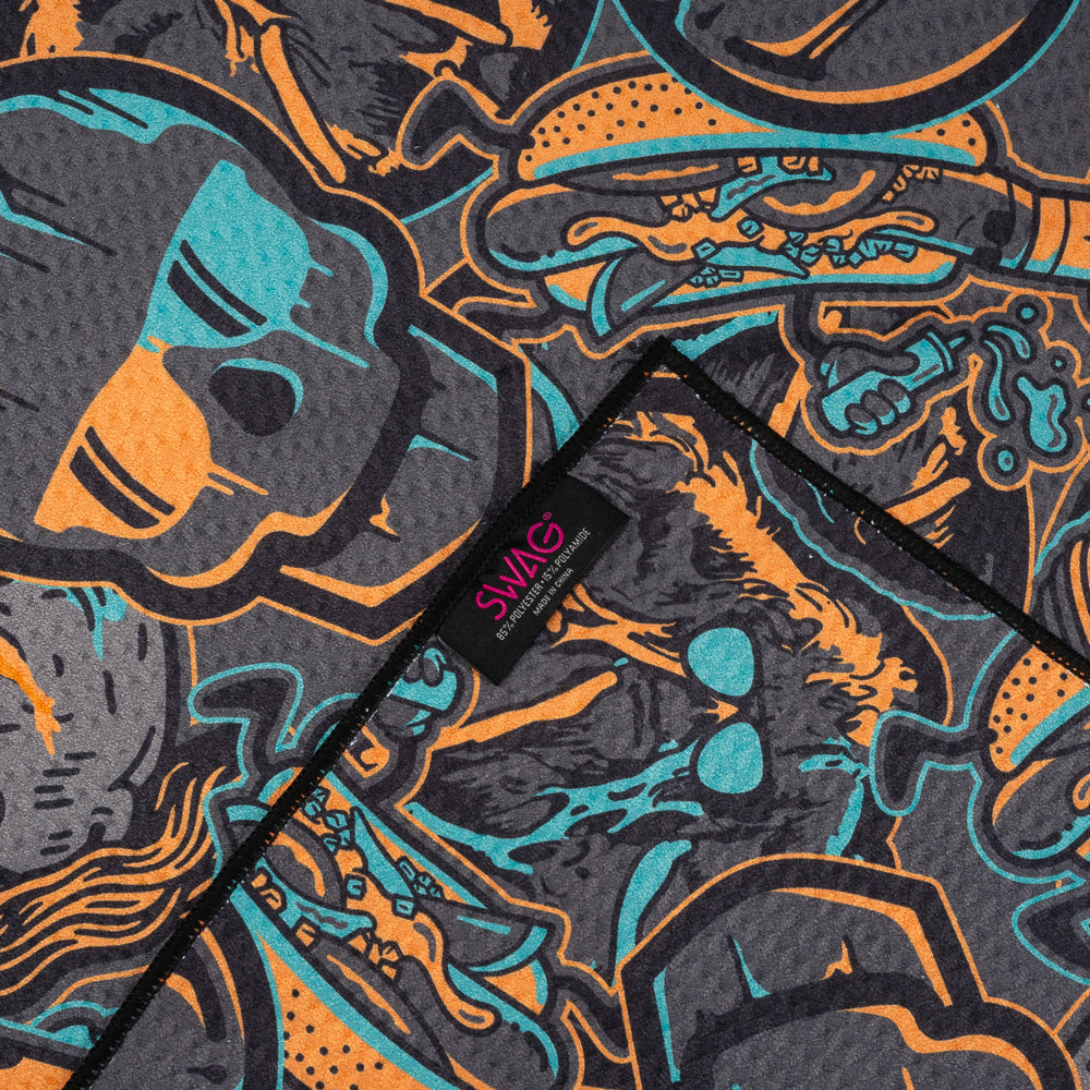 Black golf towel with all-over SWAG teal and orange “greatest hits” collage featuring skulls, kings, and graphic elements.