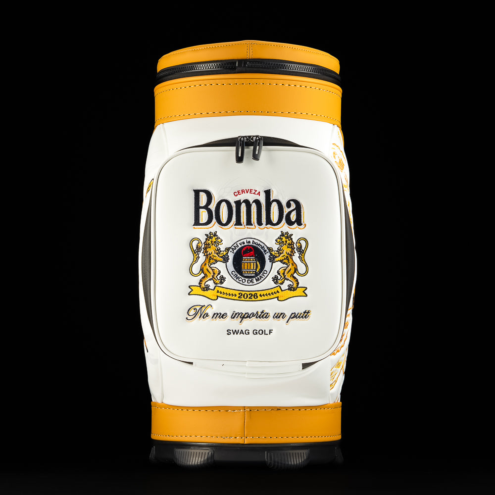 Front pocket close-up of the Bomba Den Caddy golf bag showing embroidered Bomba cerveza crest and slogan detail.