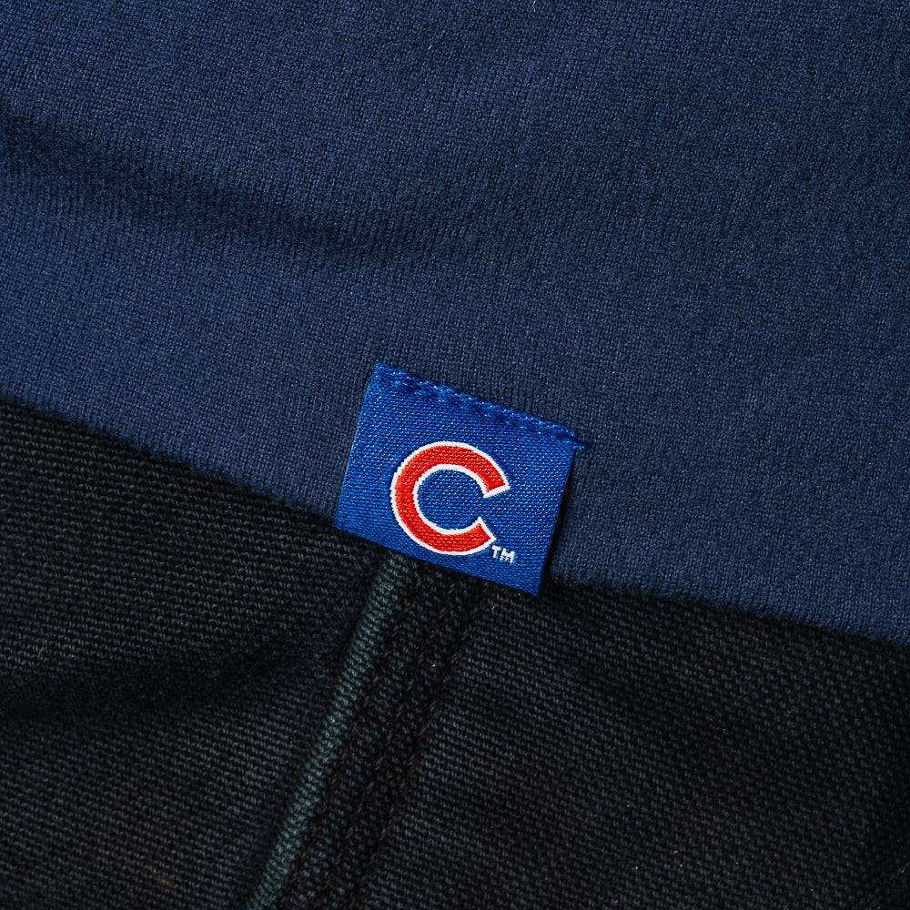 Close-up of a navy blue knit garment with a small blue fabric tag featuring a red and white circular 'C' logo, positioned over a dark woven textile.