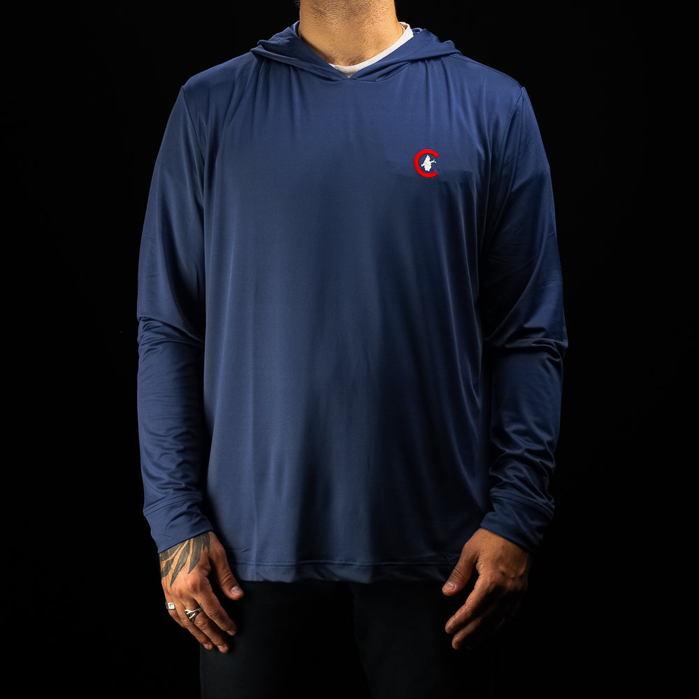 A man wearing a navy blue long-sleeve hooded performance shirt with a small red and white circular Chicago Cubs golf logo on the left chest, shown against a solid black background.