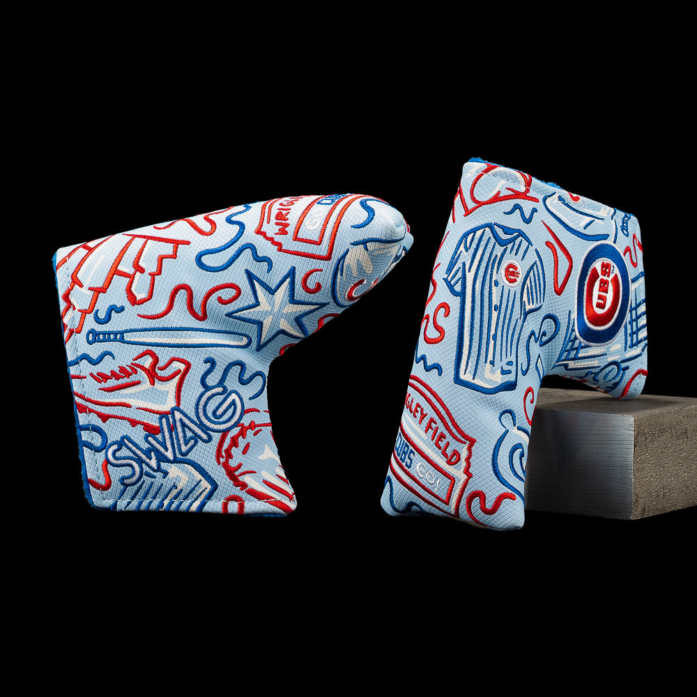 Two Chicago Cubs golf club headcovers with a light blue background and red and blue doodle-style graphics, shown against a black background with one resting on a gray block.