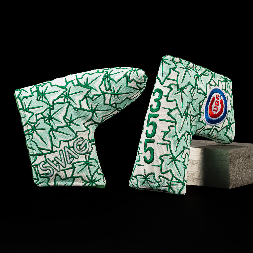 Two golf putter headcovers with a green and white starburst pattern, displayed on a black background with one resting on a gray block. One cover features the text 'SWAG' and the other displays the number '355'.