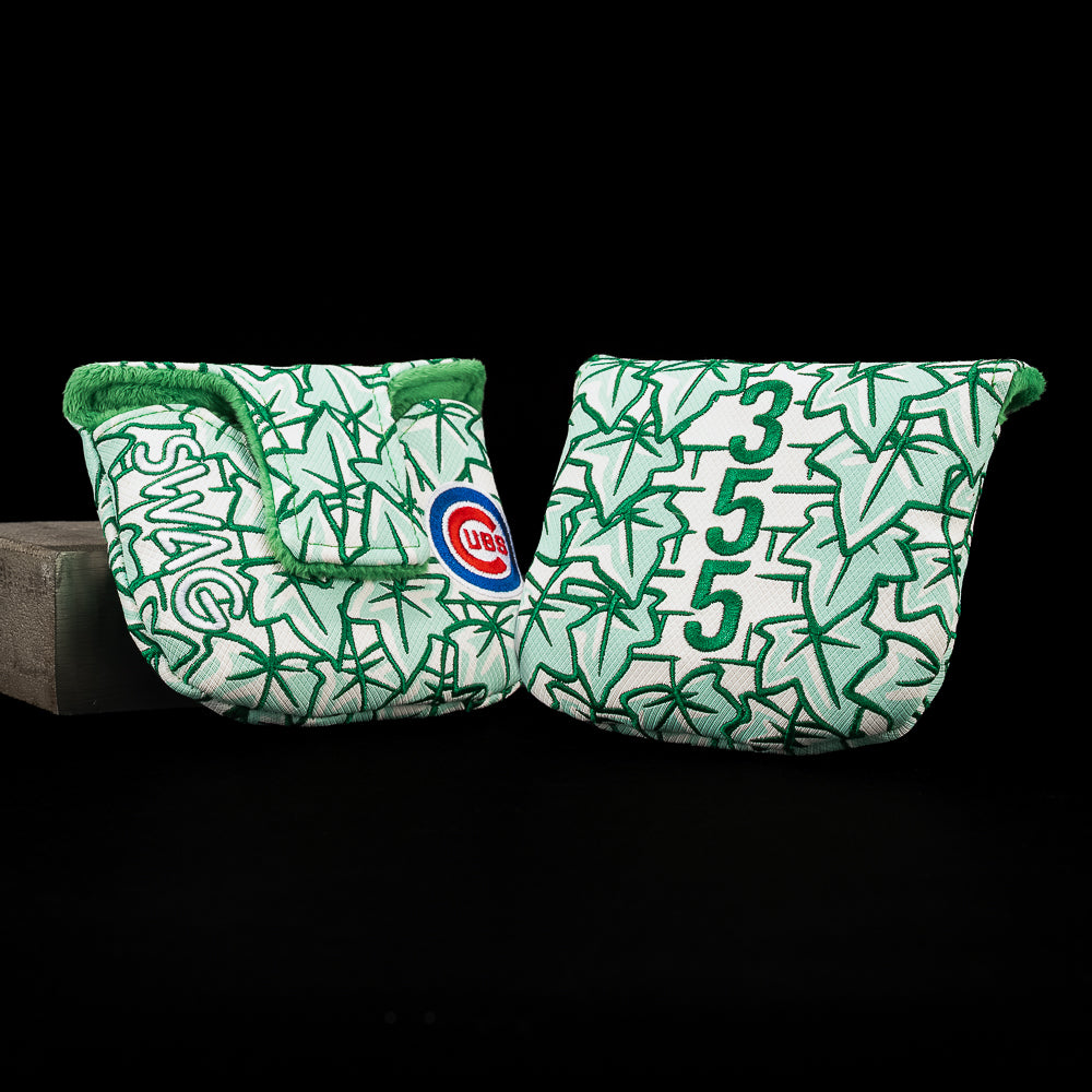 A pair of golf club headcovers in a green and white patterned design, featuring the Chicago Cubs logo and the numbers 3 and 5. One cover is resting on a dark surface against a black background, while the other is propped up against a stand.