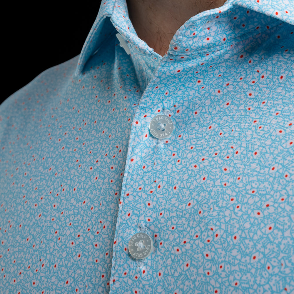 Close-up of a light blue polo shirt with a white and red dice pattern, worn by a model. The shirt features a classic collar and white-toned buttons with SWAG Golf engraving.