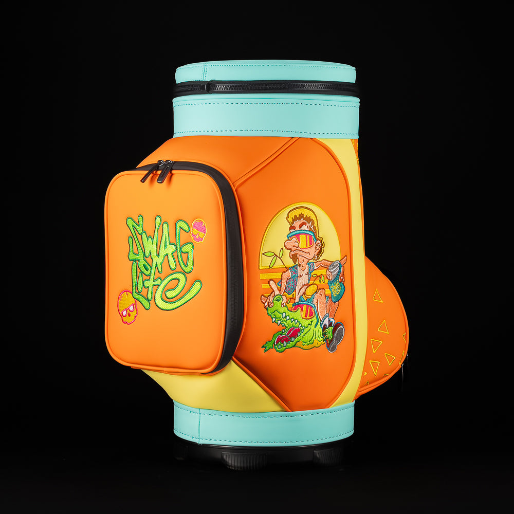 Three quarter view of SWAG Florida Man Den Caddy bag with removable aqua top lid, bold orange panels, and detailed Florida Man riding alligator embroidery.