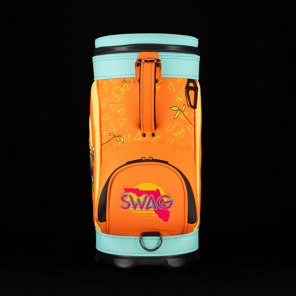 Front view of SWAG Florida Man Den Caddy bag with orange body, aqua top, black zippers, and embroidered SWAG logo over a pink Florida silhouette.