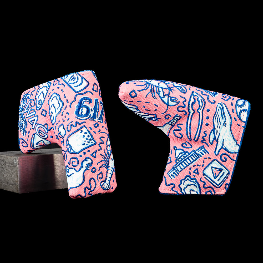 Angled front and back views of the SWAG Golf Locals Only Boston blade putter cover featuring embroidered Boston inspired artwork with waterfront landmarks, baseball inspired graphics, seafood, neighborhood icons, and city details in pink, navy, and light blue.