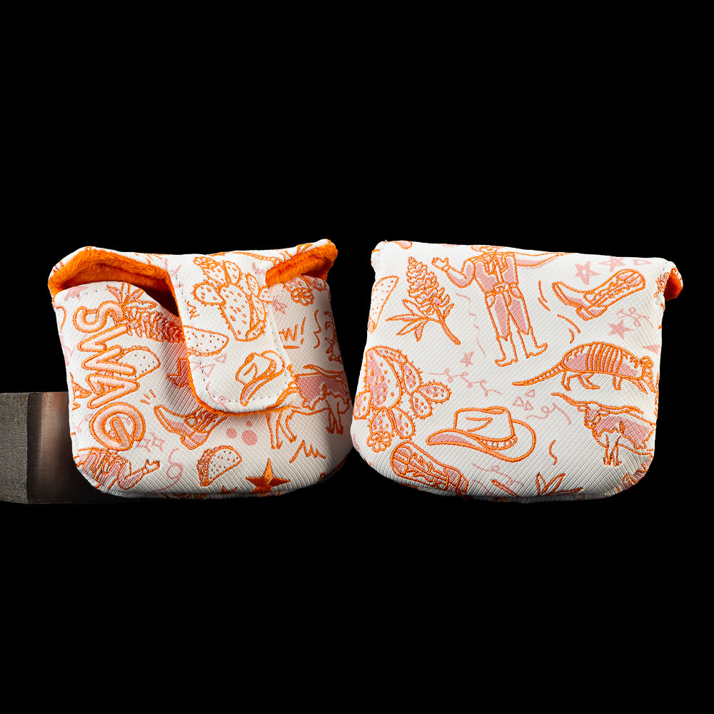 Open and closed views of the SWAG Golf Locals Only Texas blade putter cover featuring orange embroidered Texas-inspired artwork including cowboy boots, a cowboy hat, longhorns, armadillos, cacti, tacos, and Lone Star icons on a white background with an orange plush interior.