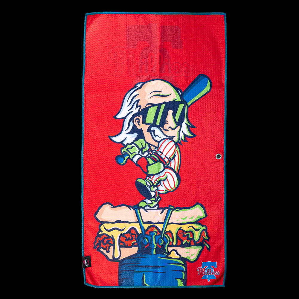 Cartoon character swinging a baseball bat while standing on a loaded Philly cheesesteak with Phillies graphics on an officially licensed Philadelphia Phillies MLB golf towel by SWAG Golf.