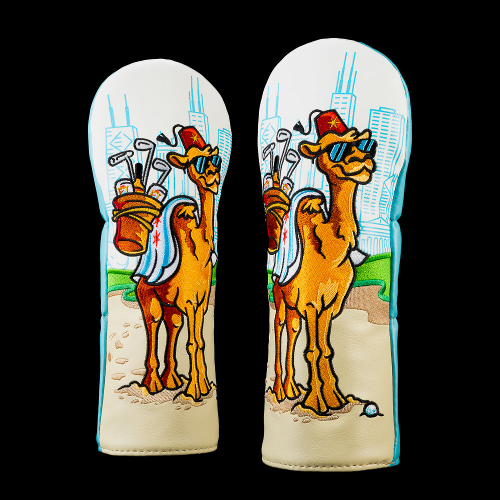 Front view of the Over the Hump fairway cover featuring a sunglasses wearing camel carrying golf clubs on a sandy course with a blue city skyline.