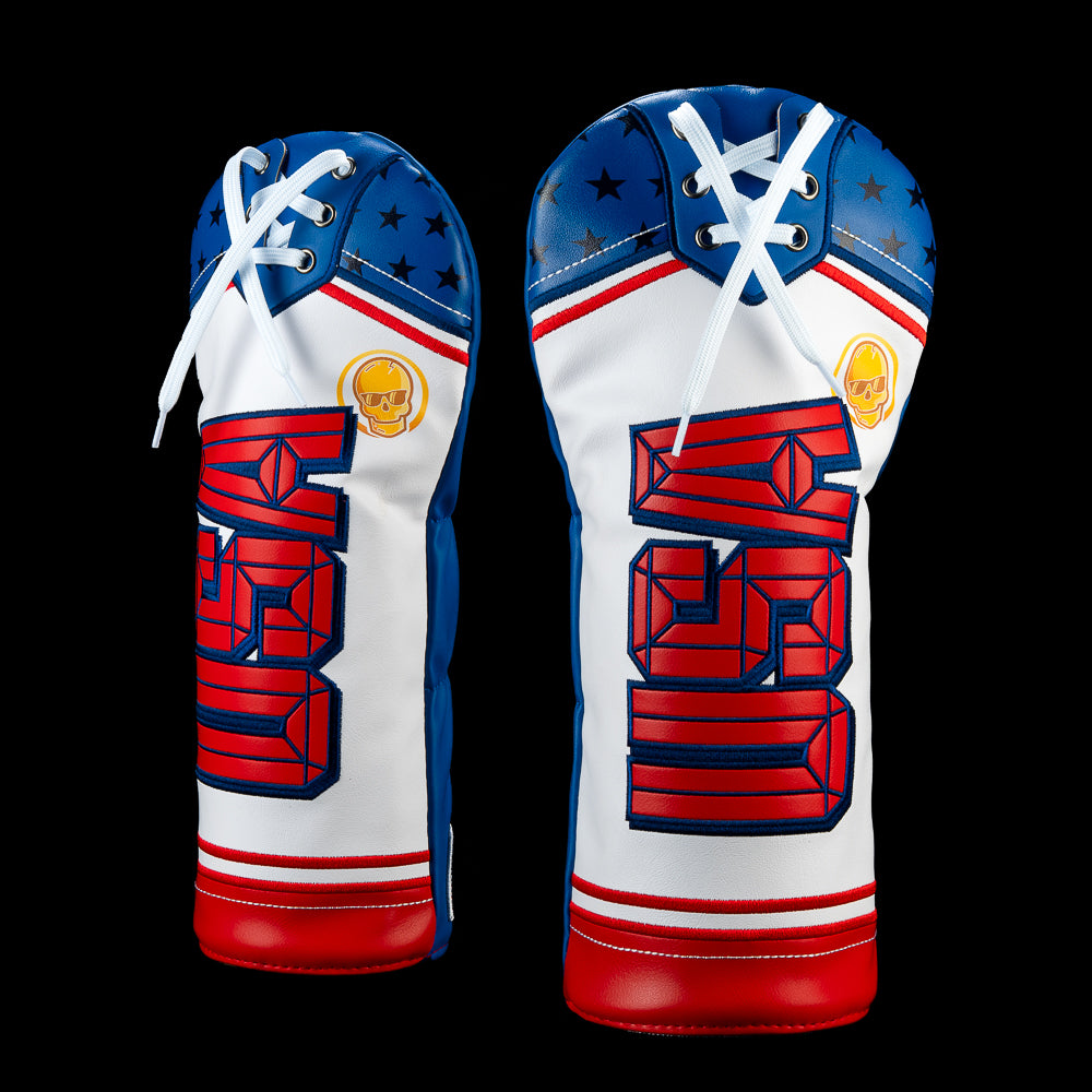 USA Sweater driver headcover with navy shoulders, white lacing, stars, red stripes, dimensional USA lettering, and a gold skull accent.