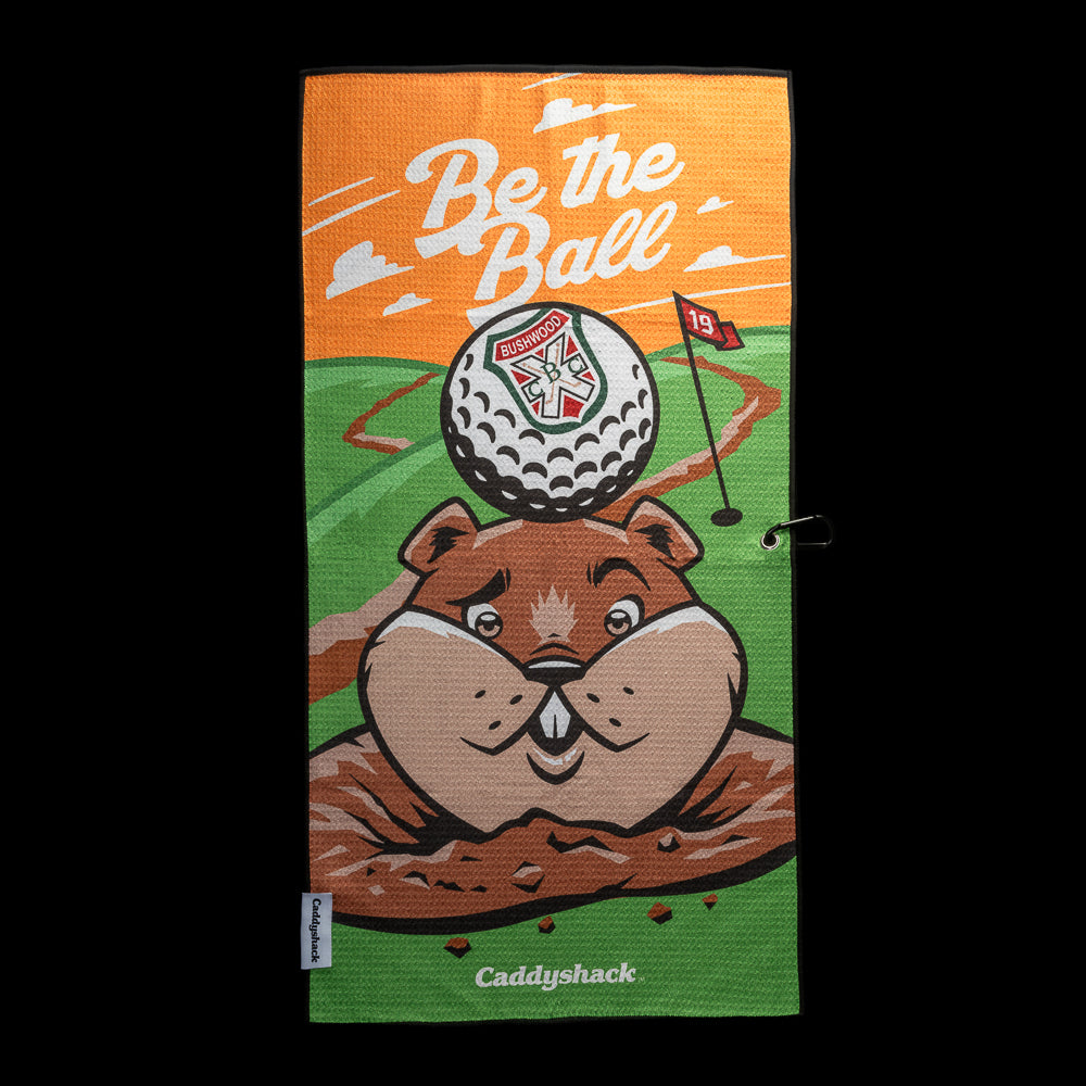 Caddyshack golf towel with white “Be the Ball” lettering, orange sky, green course, red 19 flag, and gopher balancing a Bushwood crest golf ball on its head.