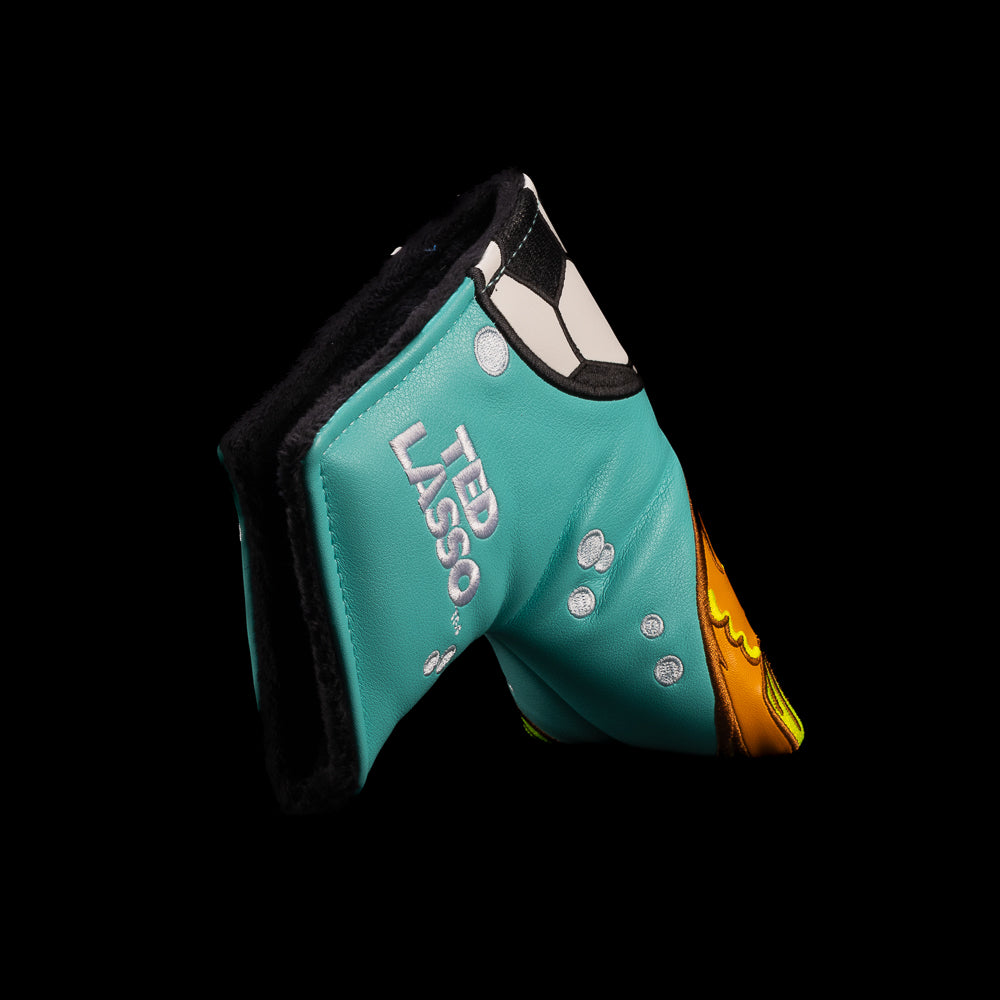 A turquoise and orange golf blade putter cover featuring a cartoon fish design and the text 'BE A GOLDFISH' on a solid black background. Officially licensed Ted Lasso design from Rewind Golf.
