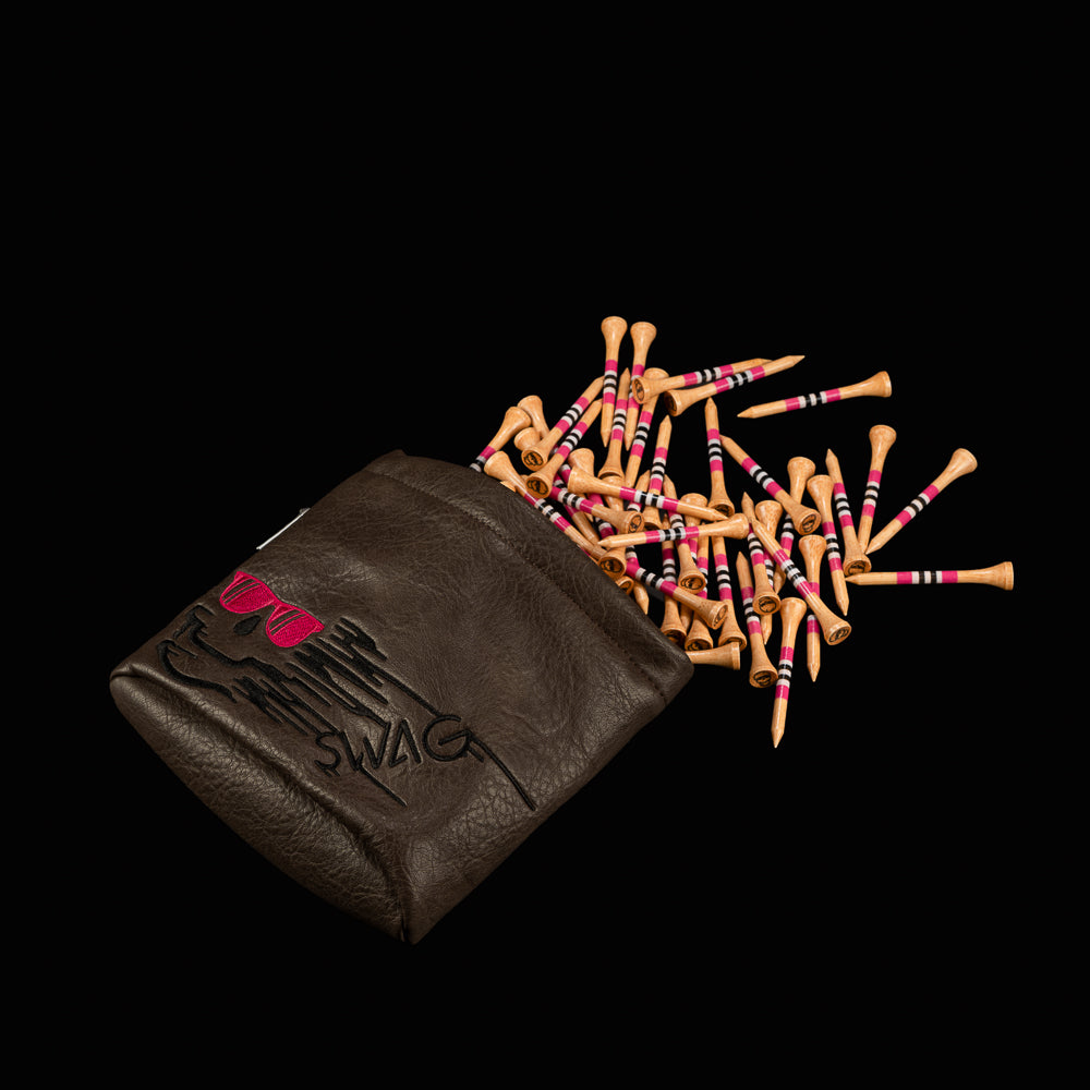 Brown vinyl SWAG golf tee pouch with embroidered skull logo wearing pink sunglasses, filled with striped wooden golf tees spilling onto a black background.