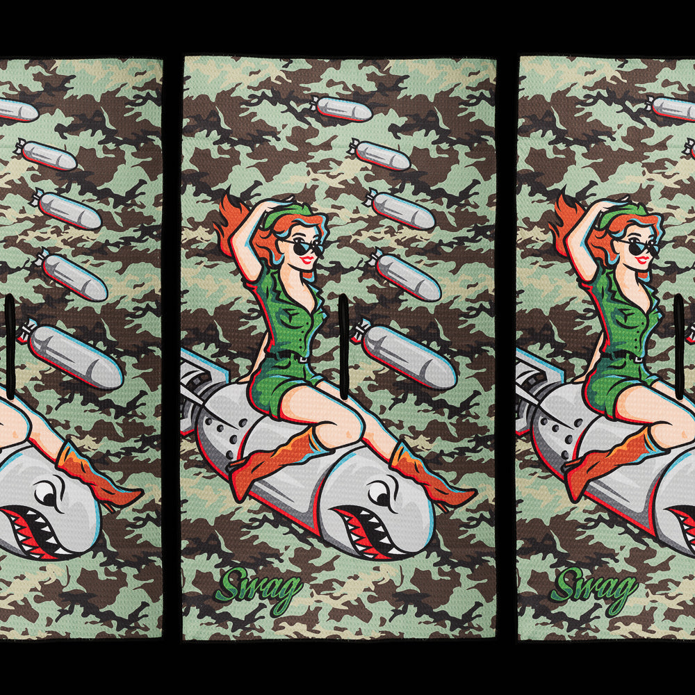 SWAG Golf Officer Bombshell golf towel featuring a vintage military pin-up riding a shark-faced bomb against a camouflage background.