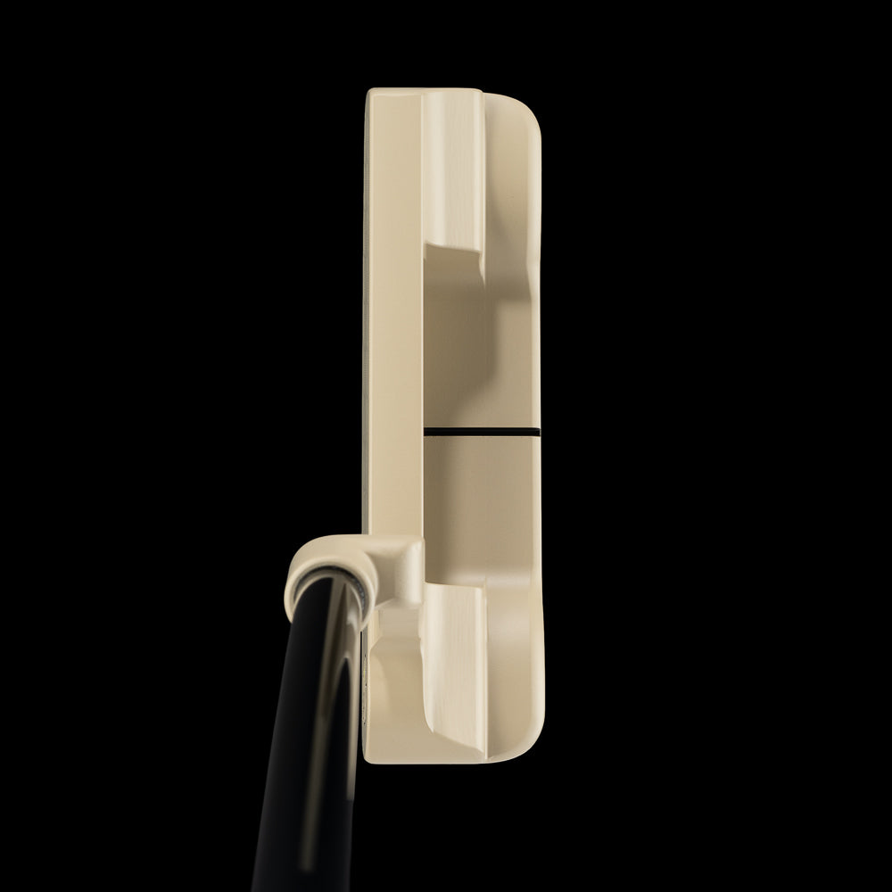 A close-up side view of a golf putter head in a warm cream color with a black shaft, set against a solid black background.