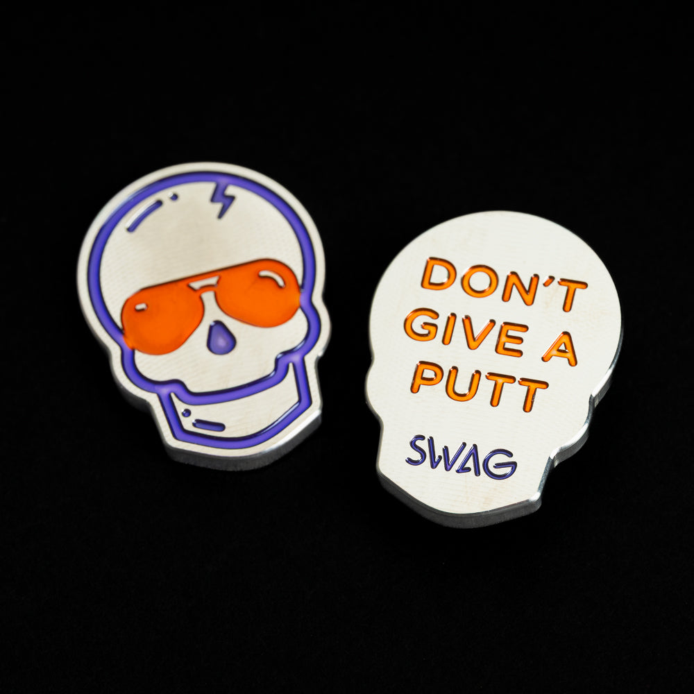 Skull-shaped silver ball marker with purple outlines, purple nose detail, orange aviator sunglasses, and "DON'T GIVE A PUTT" typography on the reverse.