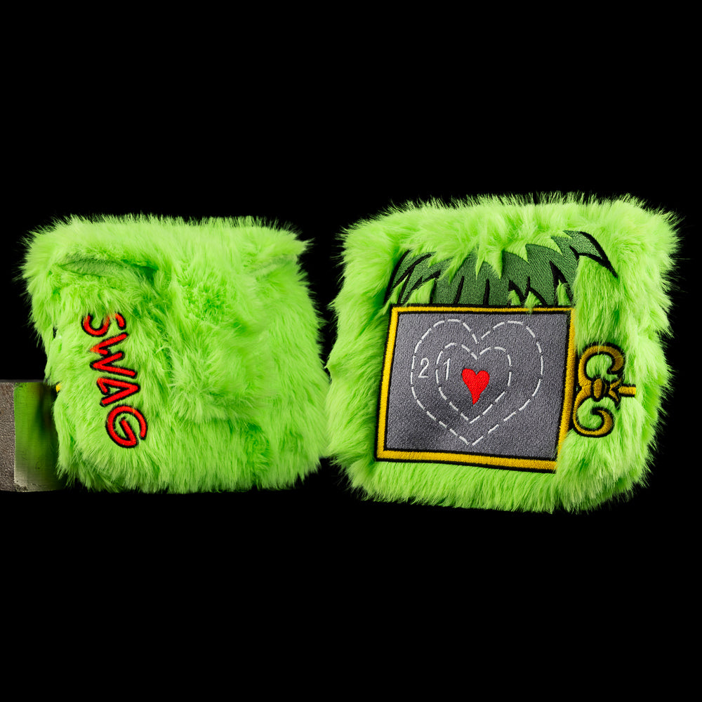 Green mallet putter cover with stitched heart graphic, messy hair illustration, and gold key accent on textured holiday pattern.