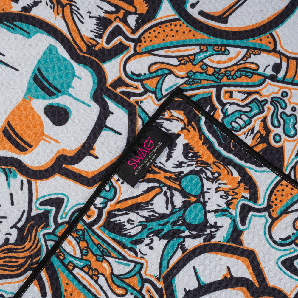 White SWAG golf towel with full-coverage teal and orange skull and king artwork in a bold graphic collage pattern.