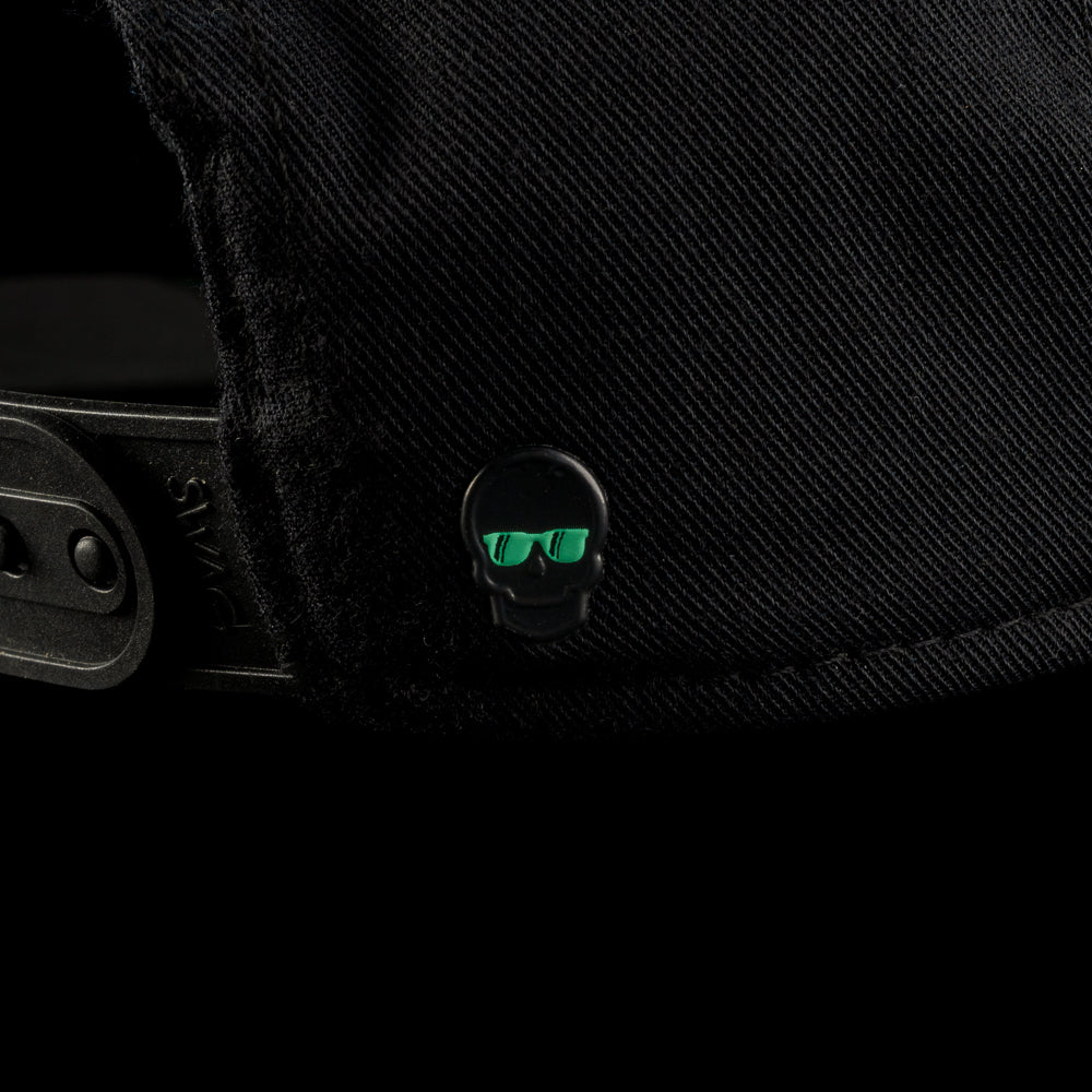 Close-up of the back of the Black Defaced Franklin hat featuring a small black skull emblem with teal sunglasses detailing near the adjustable strap.