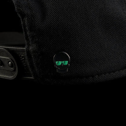 Close-up of the back of the Black Defaced Franklin hat featuring a small black skull emblem with teal sunglasses detailing near the adjustable strap.