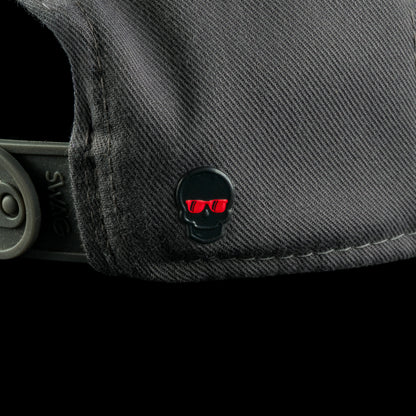 Close-up of the grey SWAGthing hat’s back panel with a small black skull emblem with red sunglasses near the adjustable strap.