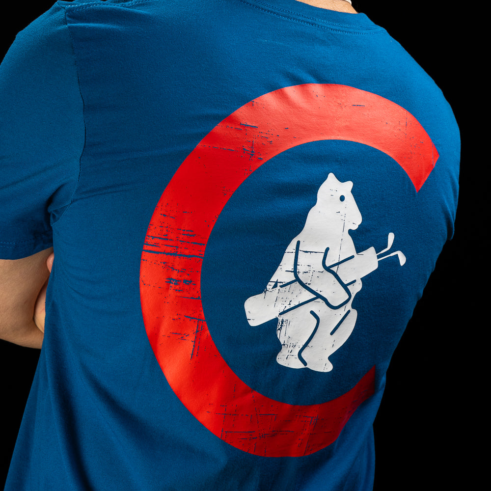 A close-up of a person wearing a blue T-shirt, showing the back of the shirt with a large distressed red circular graphic and a white bear playing golf inside the circle, against a black background.