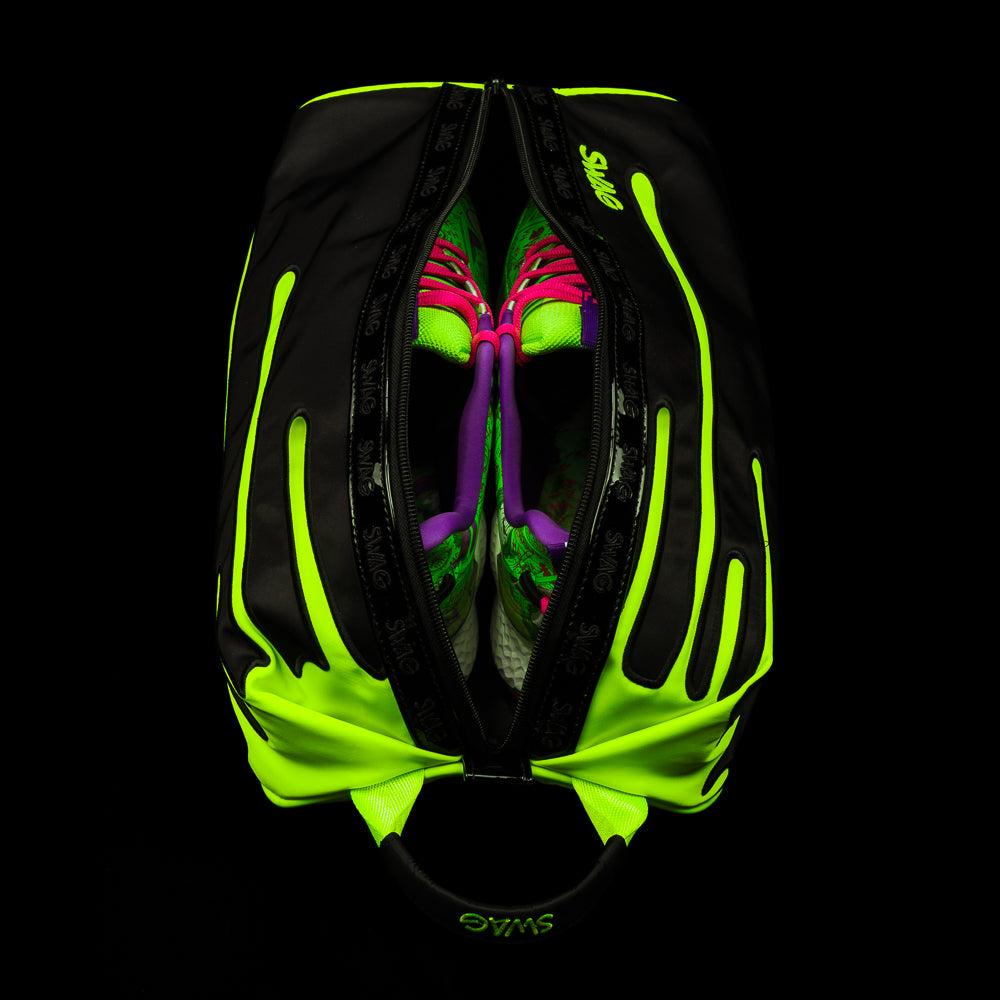 Top view of SWAG Neon Drip shoe bag opened with golf shoes inside, featuring neon drip graphics and dual zipper closure.
