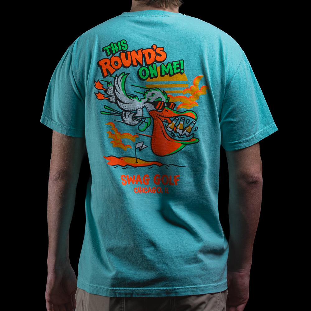 Back of aqua Pelican T-Shirt with large pelican graphic and text “This Round’s On Me!” above SWAG Golf Chicago, IL.