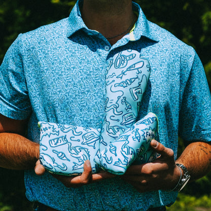Person wearing a blue patterned polo shirt holding matching golf headcovers.