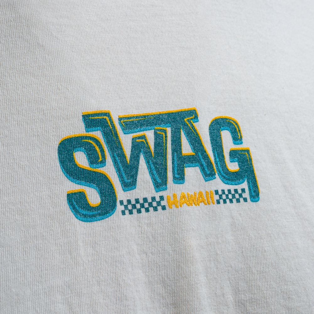 Close-up of SWAG Hawaii logo in teal and yellow on cream cotton t-shirt.