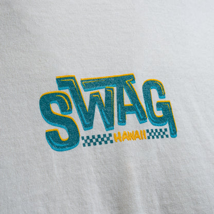 Close-up of SWAG Hawaii logo in teal and yellow on cream cotton t-shirt.