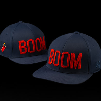 Front angled view of the BOOM hat featuring bold red embroidered BOOM lettering on a navy performance cap with a structured crown and curved brim.
