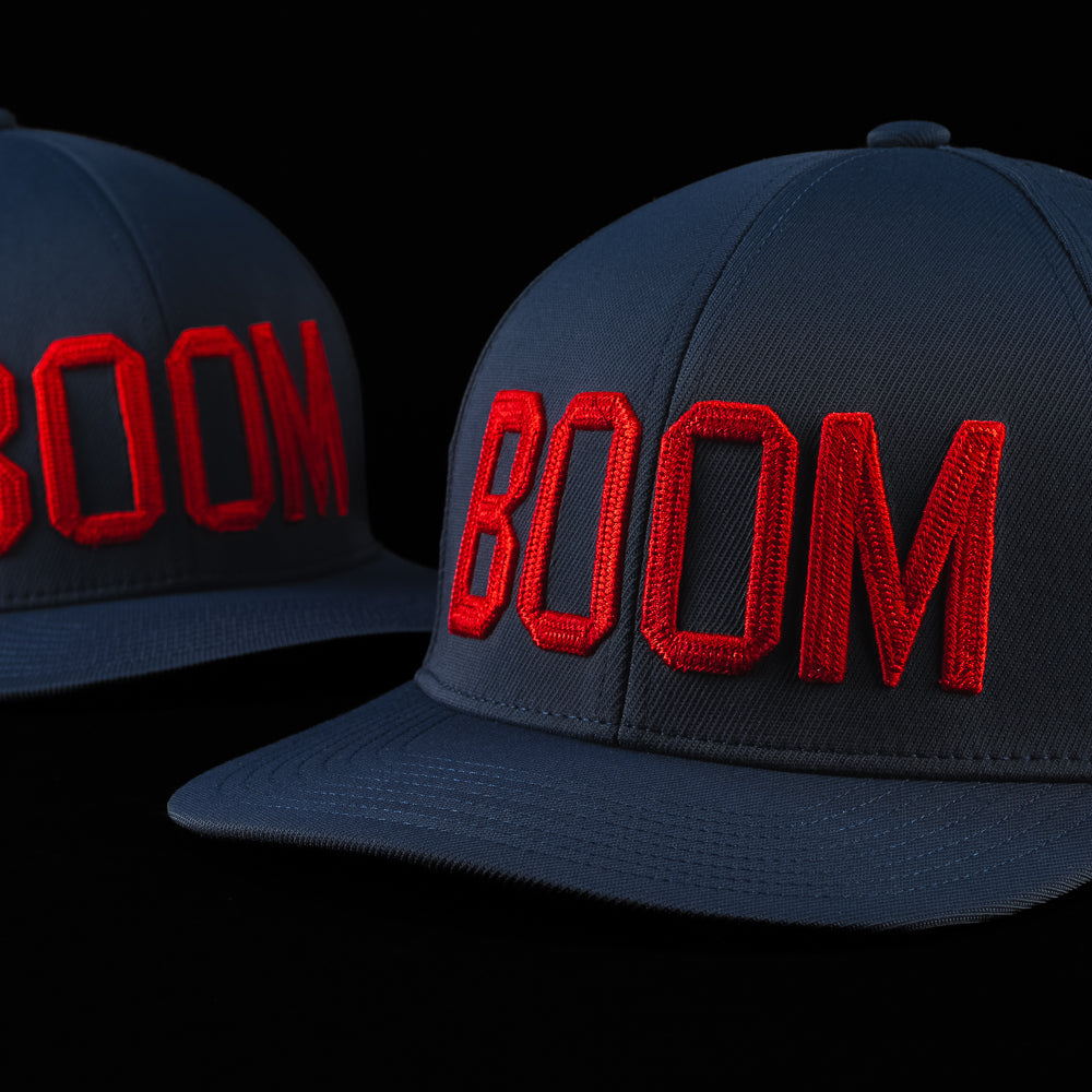 Side view of the BOOM hat showcasing oversized red embroidered BOOM lettering on a navy blue cap with a curved brim.