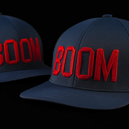Side view of the BOOM hat showcasing oversized red embroidered BOOM lettering on a navy blue cap with a curved brim.