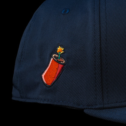 Close-up detail of the BOOM hat featuring an embroidered firecracker graphic on the side panel of the navy blue cap.