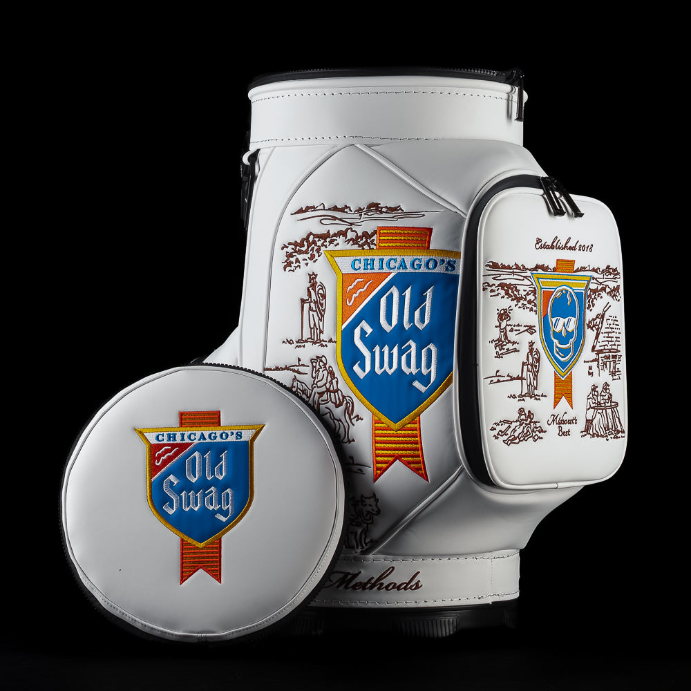Front three-quarter view of the white Old SWAG Den Caddy Cooler featuring a large blue, red and gold shield logo, vintage Chicago illustrations and detachable round lid.