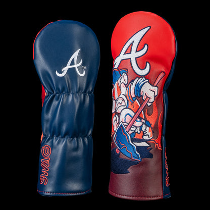 Back and front view of an Atlanta Braves fairway cover. The back features the embroidered Braves "A" logo on a navy panel. The front showcases a cartoon Braves mascot wearing mirrored sunglasses and headphones while gripping a tomahawk, set beneath an oversized Braves "A" against a fiery red background.