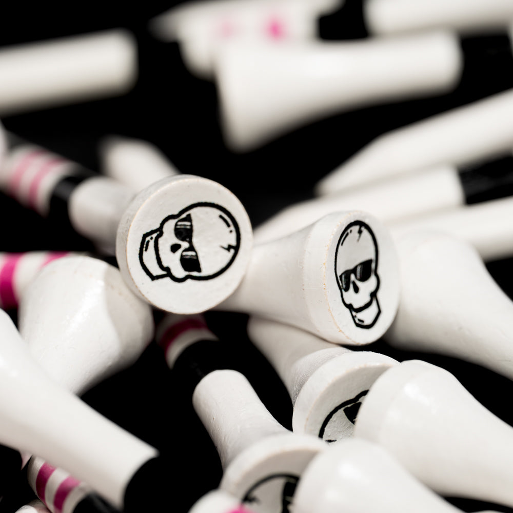 Close-up of white SWAG Golf tees featuring black skull logo graphics with pink and black striped detailing.