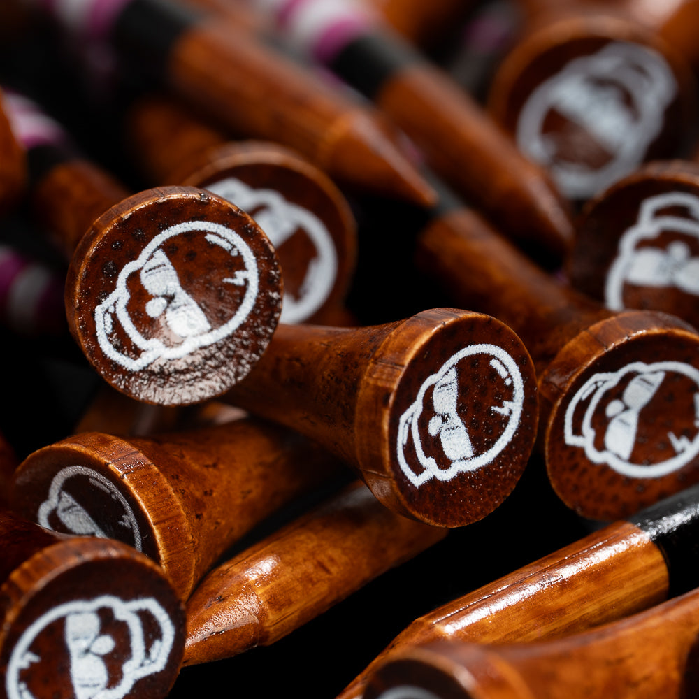 Close-up of premium brown wooden SWAG Golf tees featuring white skull logo detailing and pink stripe accents.