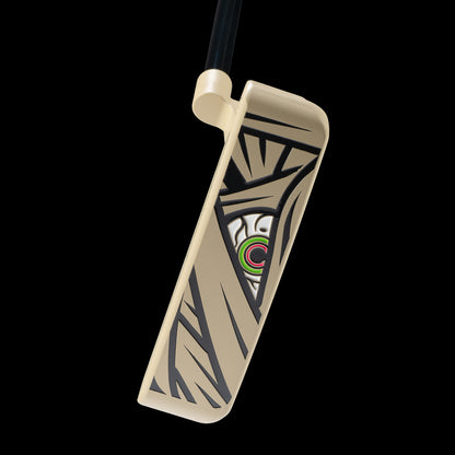 A close-up studio shot of a golf putter head on a black background, featuring a cream-colored face with black mummy graphics and a central logo containing green, pink, white, and black.