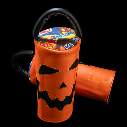 An orange Halloween-themed cylindrical driver headcover with a black handle, featuring a stitched jack-o'-lantern face on the front. A second view shows the open interior lined with colorful candy illustrations.