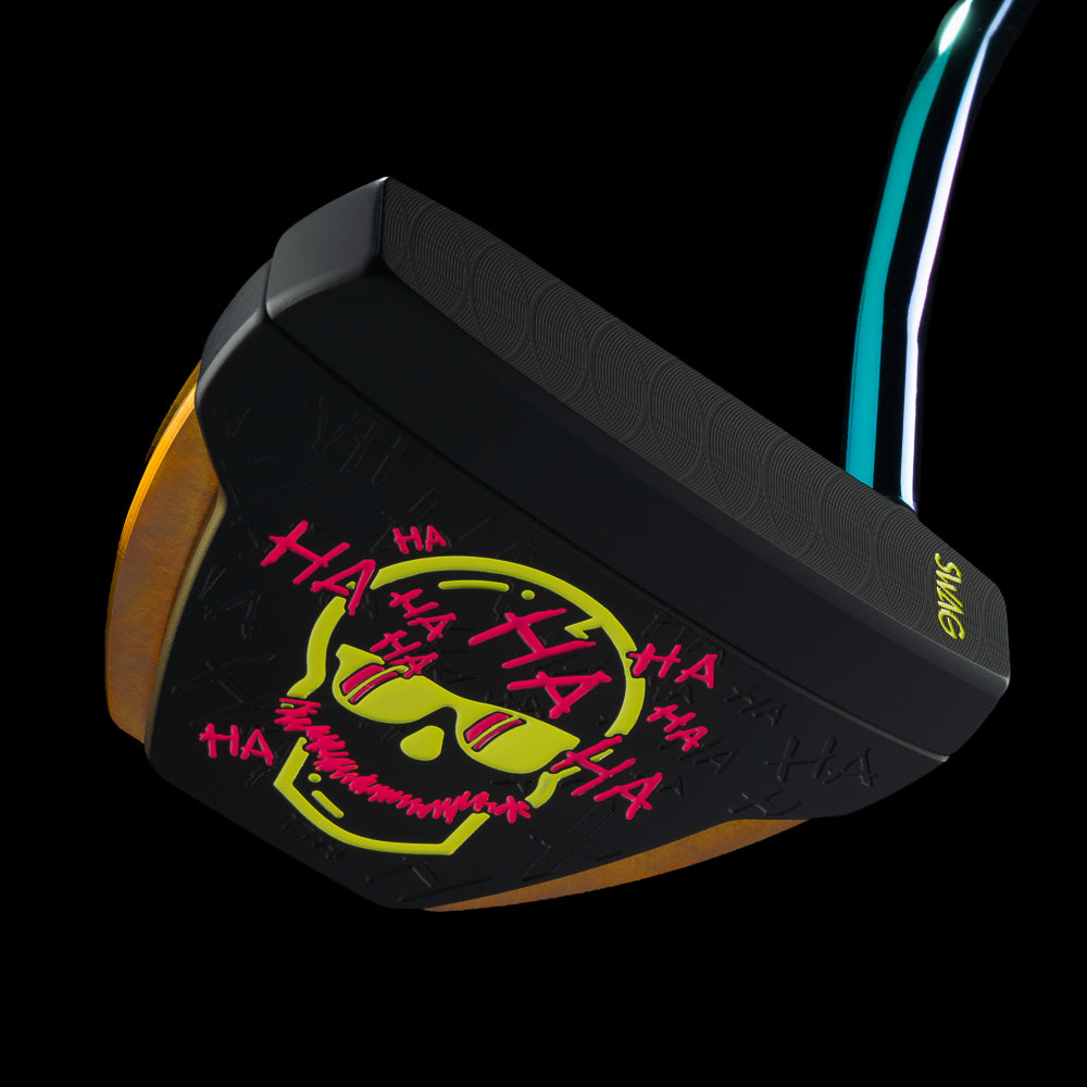 A close-up studio shot of a golf putter head on a black background, featuring a black face with a yellow and pink graffiti-style skull graphic and the word 'HAHAHA' in pink, plus a teal and white shaft visible behind it.
