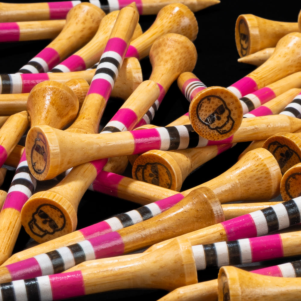 Close-up of SWAG Golf wooden tees featuring pink, black, and white striped shafts and skull-branded heads.