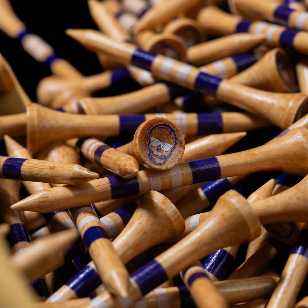 Close-up of the tan Taco Bell x SWAG Golf golf tees with purple bands and skull logo details.