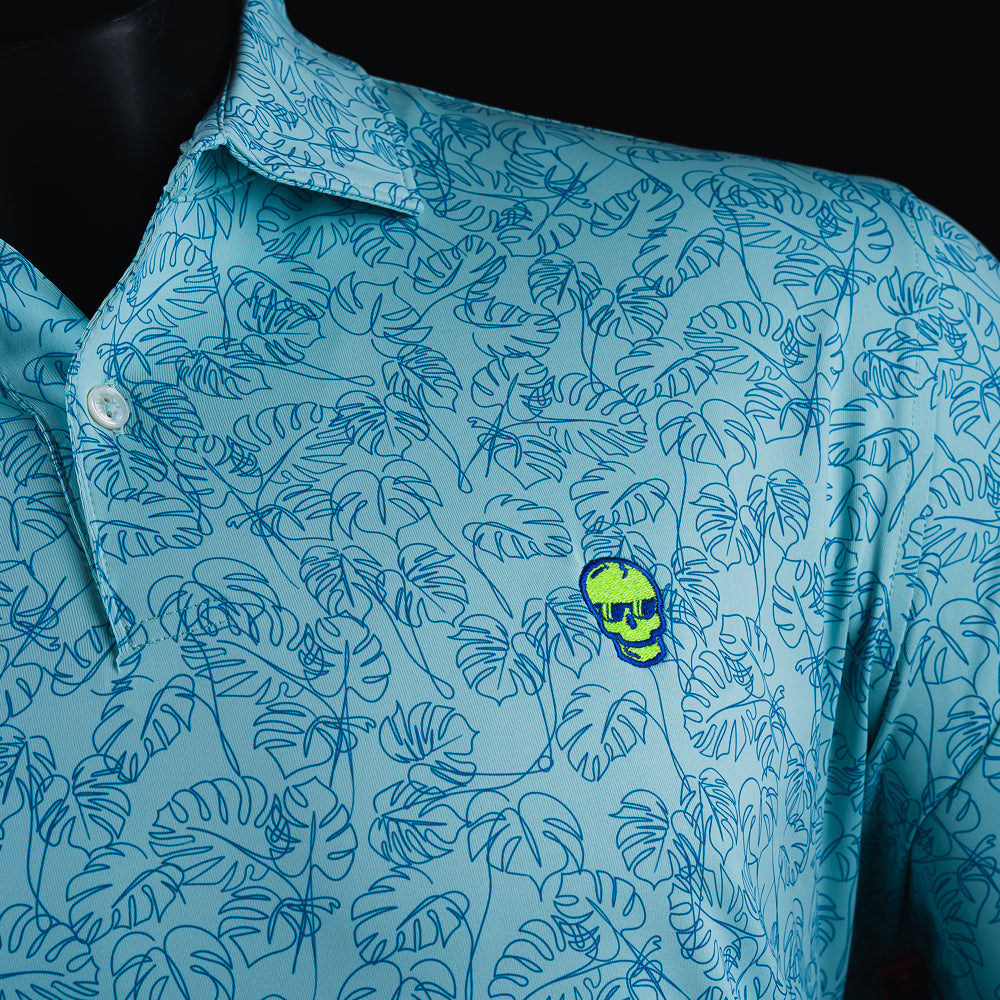 Swag x Peter Millar with an embroidered green Skull on a blue palm leaf print men's short sleeve golf polo shirt.