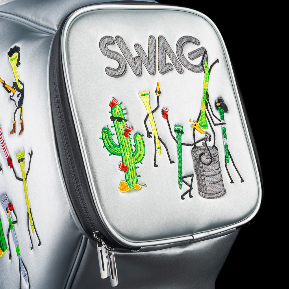 Close-up of front pocket on silver SWAG Golf Desert Tee Party Den Caddy showing embroidered cactus characters and golf tees beneath SWAG logo.